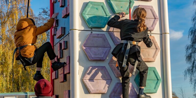 Two school children scaling a mobile climbing wall outside
