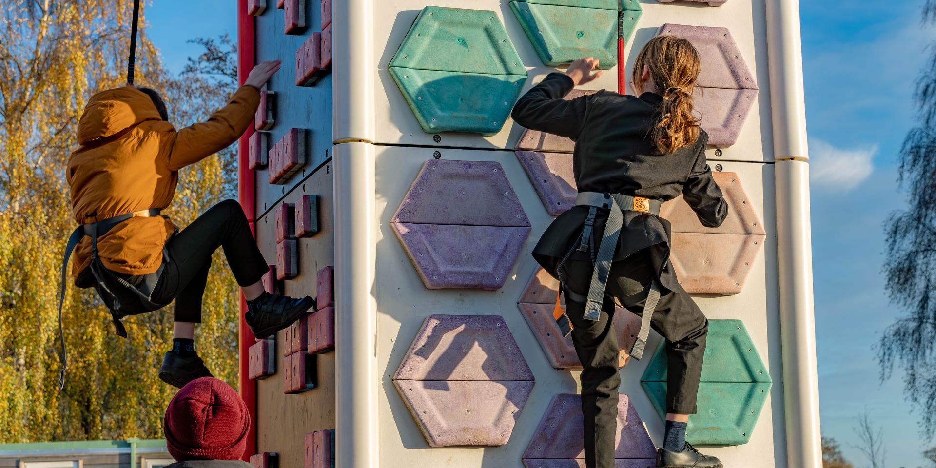 Two school children scaling a mobile climbing wall outside