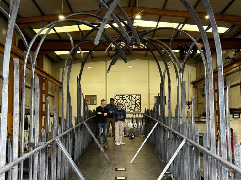 three colleagues standing beneath a piece of newly constructed metal bridge in a workshop