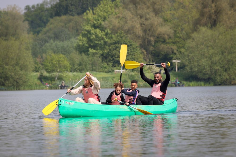 Happy mum, dad and two children in a green canoe with yellow paddles on a lake