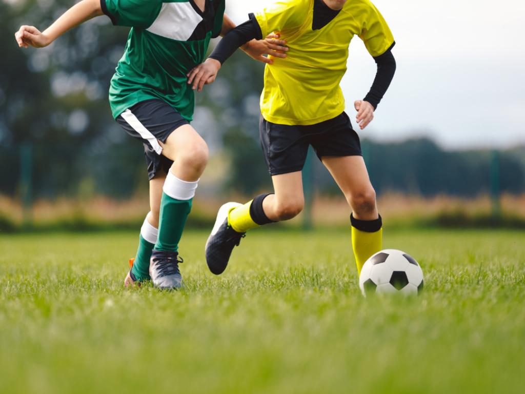two football players chasing a football on a green grass pitch