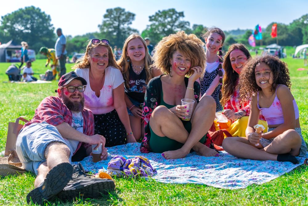 Group of young people on a picnic blanket on a green field on a sunny day