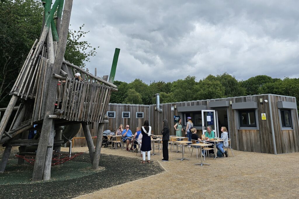 Wooden play area next to a small cafe situated in a wooden clad container, with seating outside