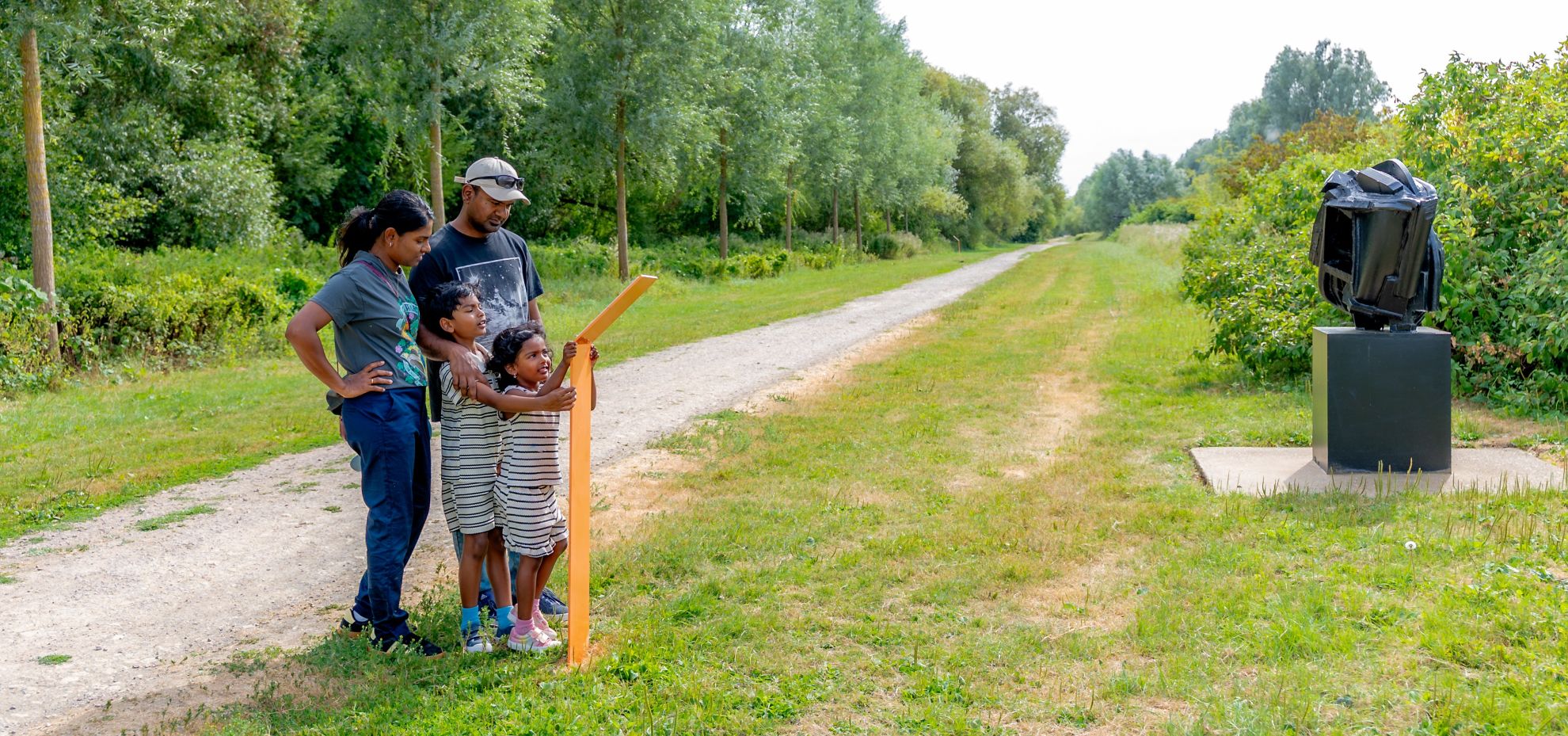 Mum, dad and young son and daughter reading a sculpture information board in a country park