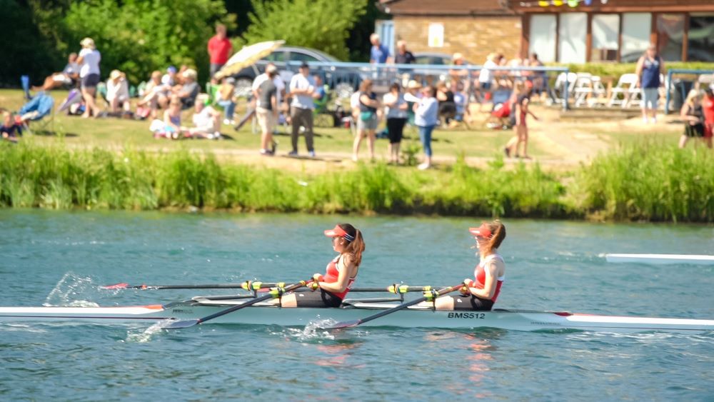 two women rowing on a lake with spectators in the background