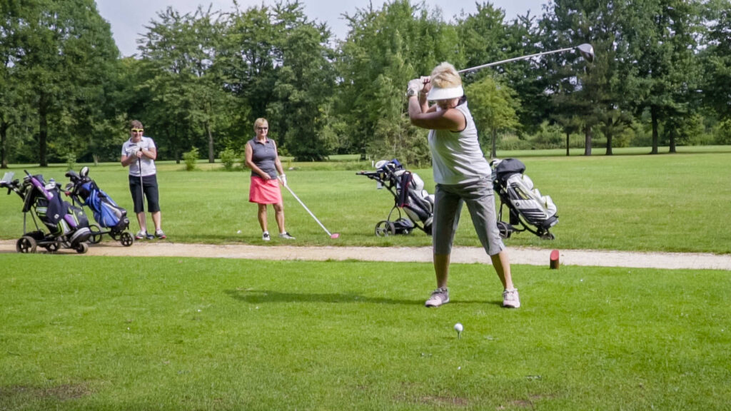 Woman about to take a golf shot with other golfers behind.