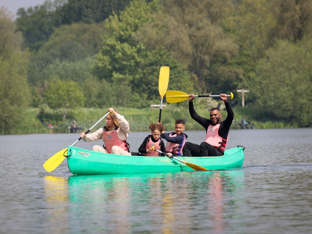 Mum, dad, young son and daughter having fun in a green canoe on a lake with yellow paddles