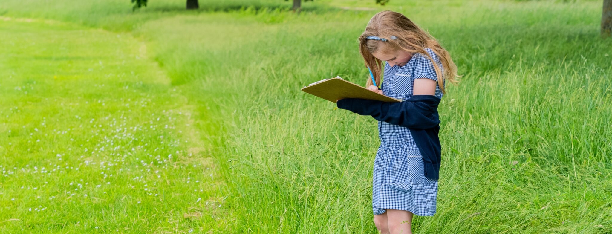 girl in blue school uniform standing in a green grass field with a clipboard