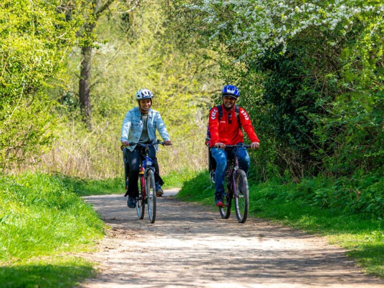 couple cycling along a path in a country park with trees either side