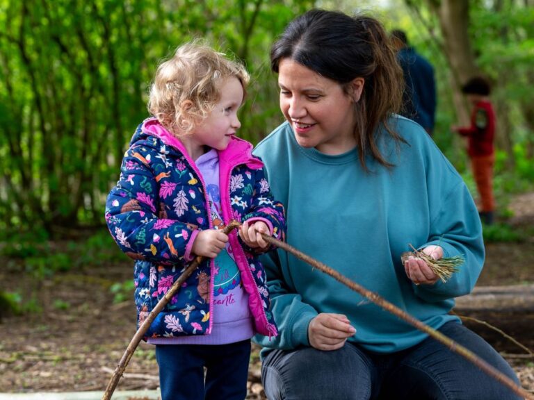 mum and young daughter outside in the autumn enjoying playing with sticks