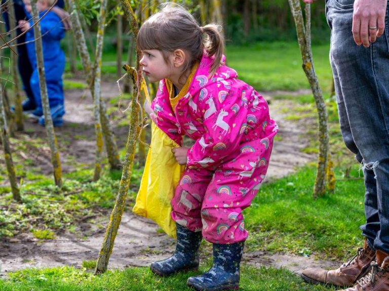 Young girl in a pink rain suit and wellies playing outside