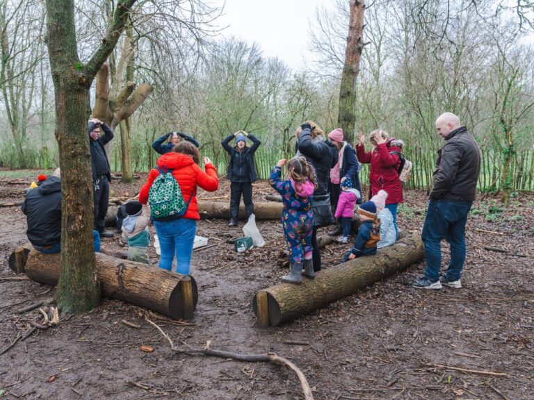 Group of parents and young toddlers playing a game in a circle in the woods