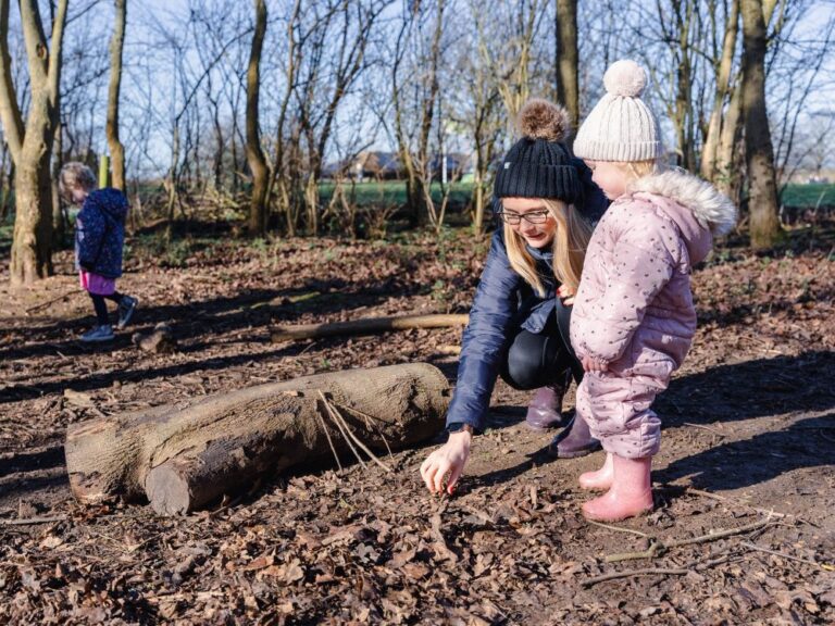 Mum and toddler daughter in winter clothing playing in the woods