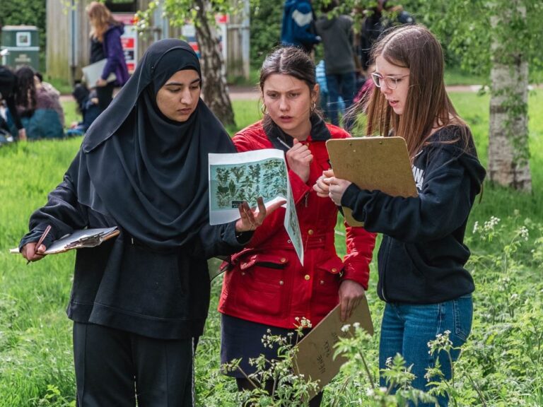 three teenage girls working on clipboards outside on a school visit