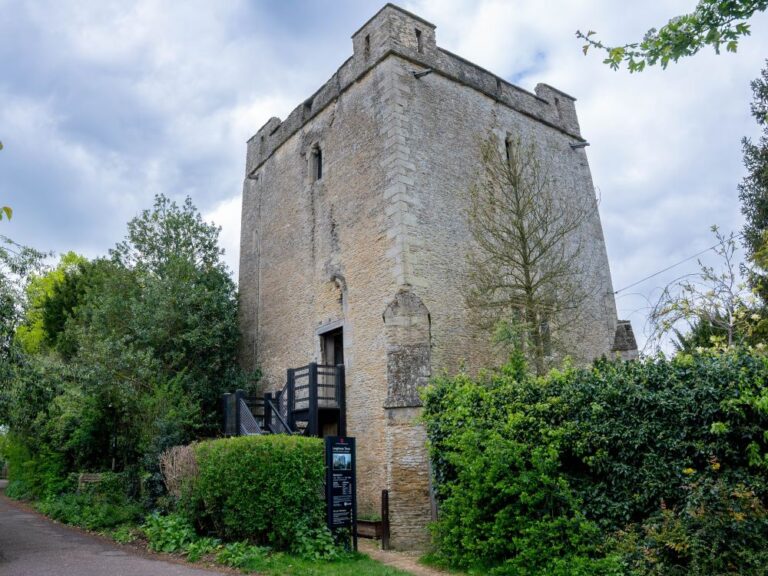 Full view of the impressive stone Longthorpe Tower with wooden staircase to the door and green trees around the edges