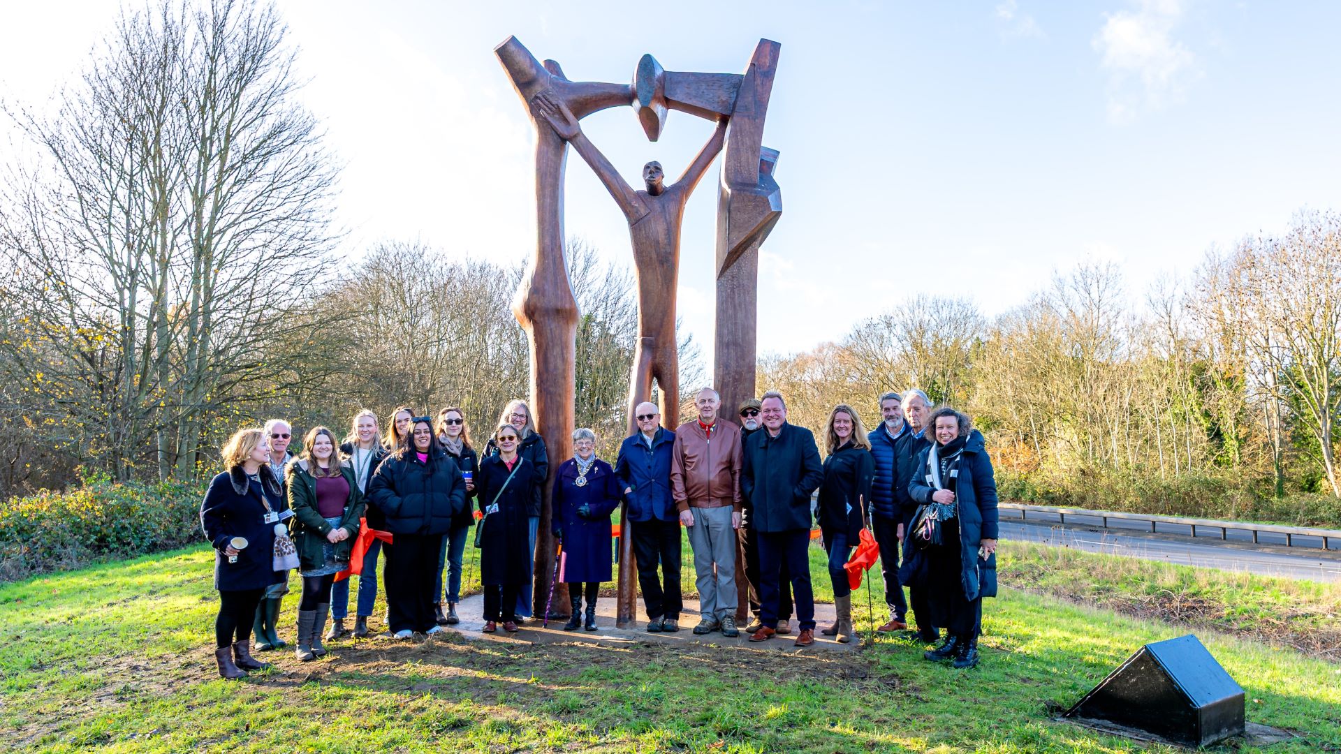 Group of staff and community members gather beneath the Peterborough Arch sculpture to celebrate.