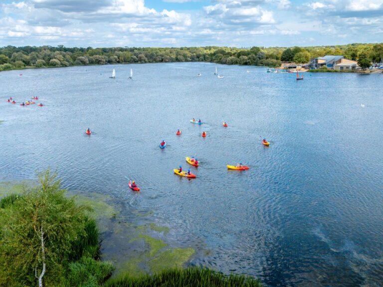 drone shot of a large lake in a country park with lots of people kayaking in it