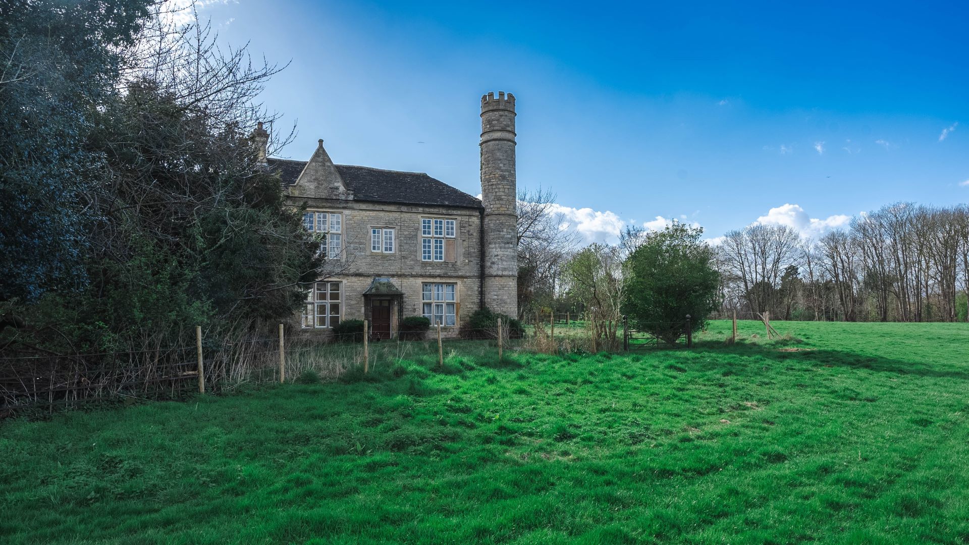 An impressive stone house with a turret surrounded by a green field and trees