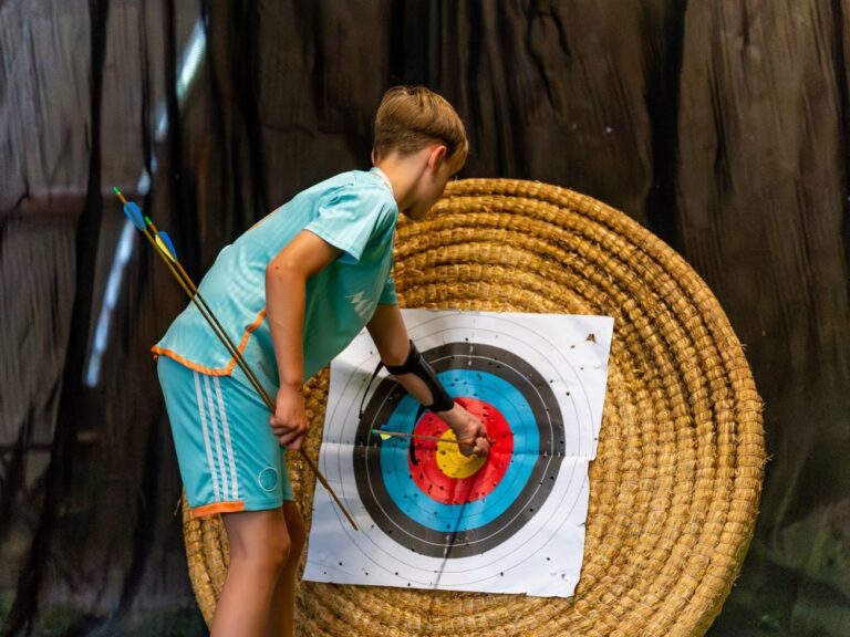 boy wearing a sky blue football kit taking an arrow out of an archery target