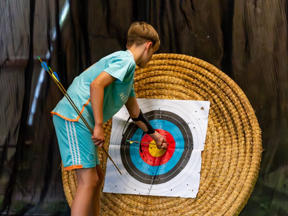 teen boy wearing a football kit taking an arrow out of an archery target