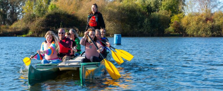 Group of adults paddling a green bell boat on a lake