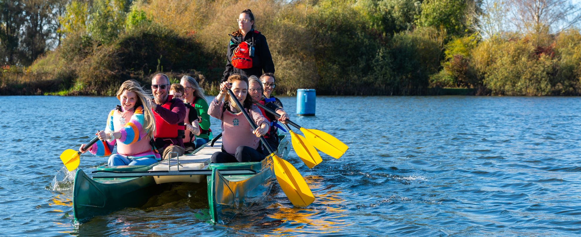 Group of adults paddling a green bell boat on a lake