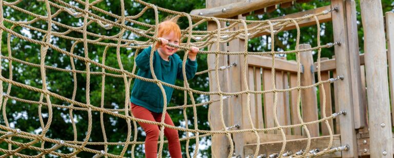 Young boy with red hair and a green jumper inside a rope bridge in a play park