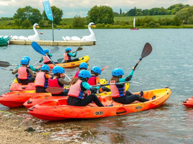 Group of children setting sail in some red and yellow canoes on a lake