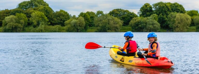 two boys in a red and yellow canoe sailing in a lake with trees in the background