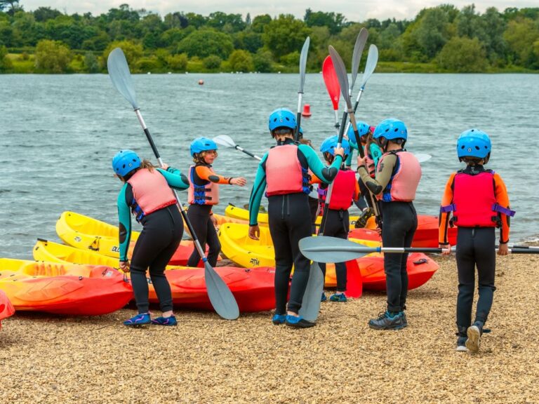 group of school children wearing wetsuits and carrying paddles getting ready to go kayaking on a lake