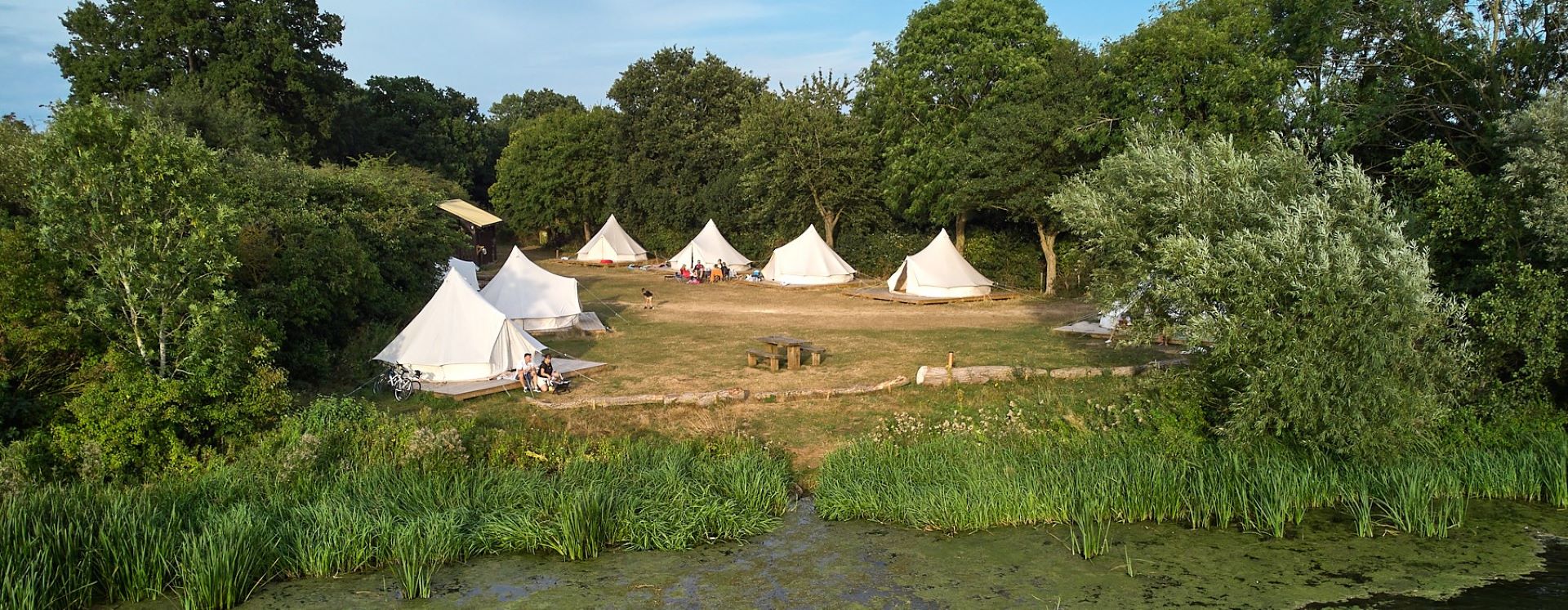 a peaceful campsite featuring 8 white bell tents on the shore of a lake surrounded by trees