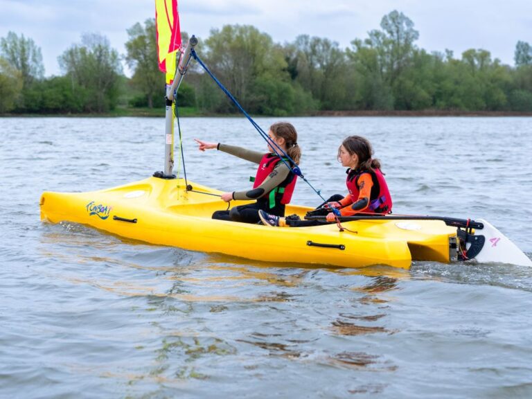 two girls wearing life jackets in a yellow sailing boat on a lake