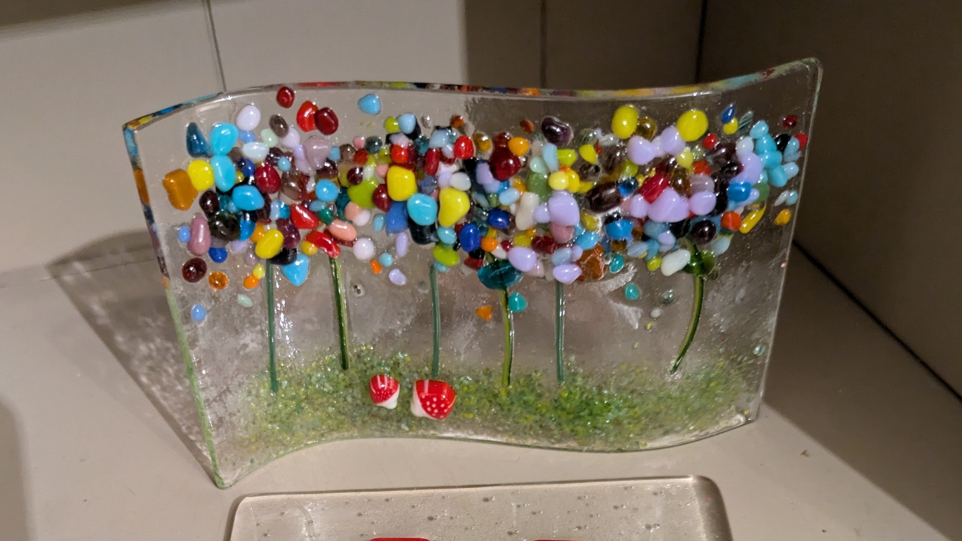 A wavy piece of translucent glass features a handmade design of beautiful wildflowers from a variety of colourful stones and other elements of glass.