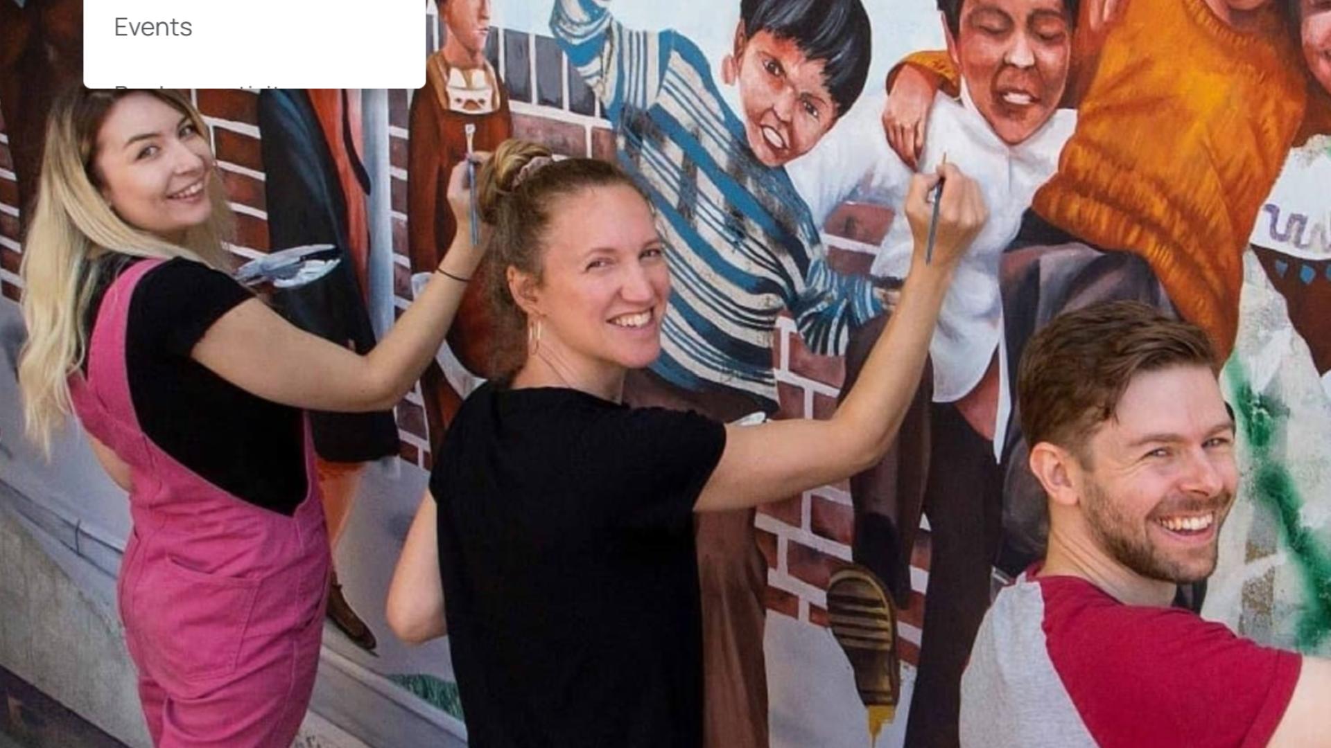 Three young artists painting a colourful wall mural of children