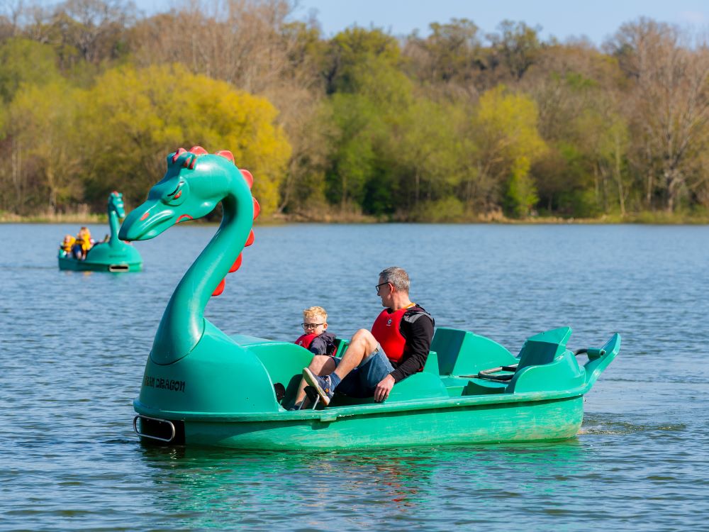 father and young son in a green dragon pedalo boat on a lake
