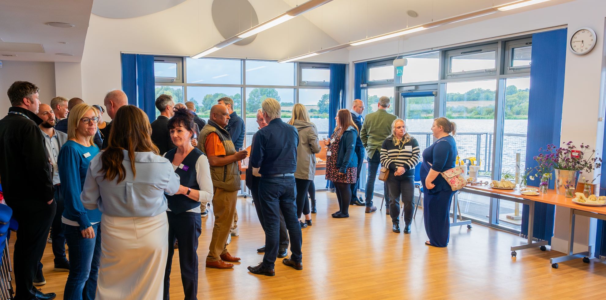 A networking event taking place in a spacious meeting room with full length windows looking out onto the lake