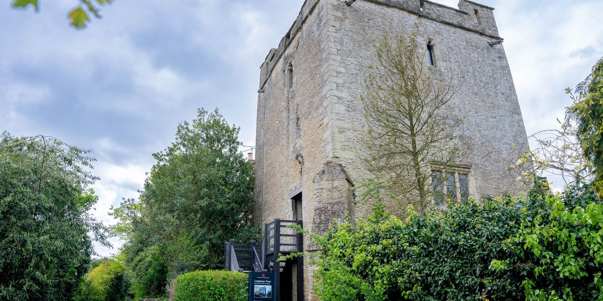 A tall Medieval stone tower with wooden steps on the left hand side and trees surrounding the bottom of the tower