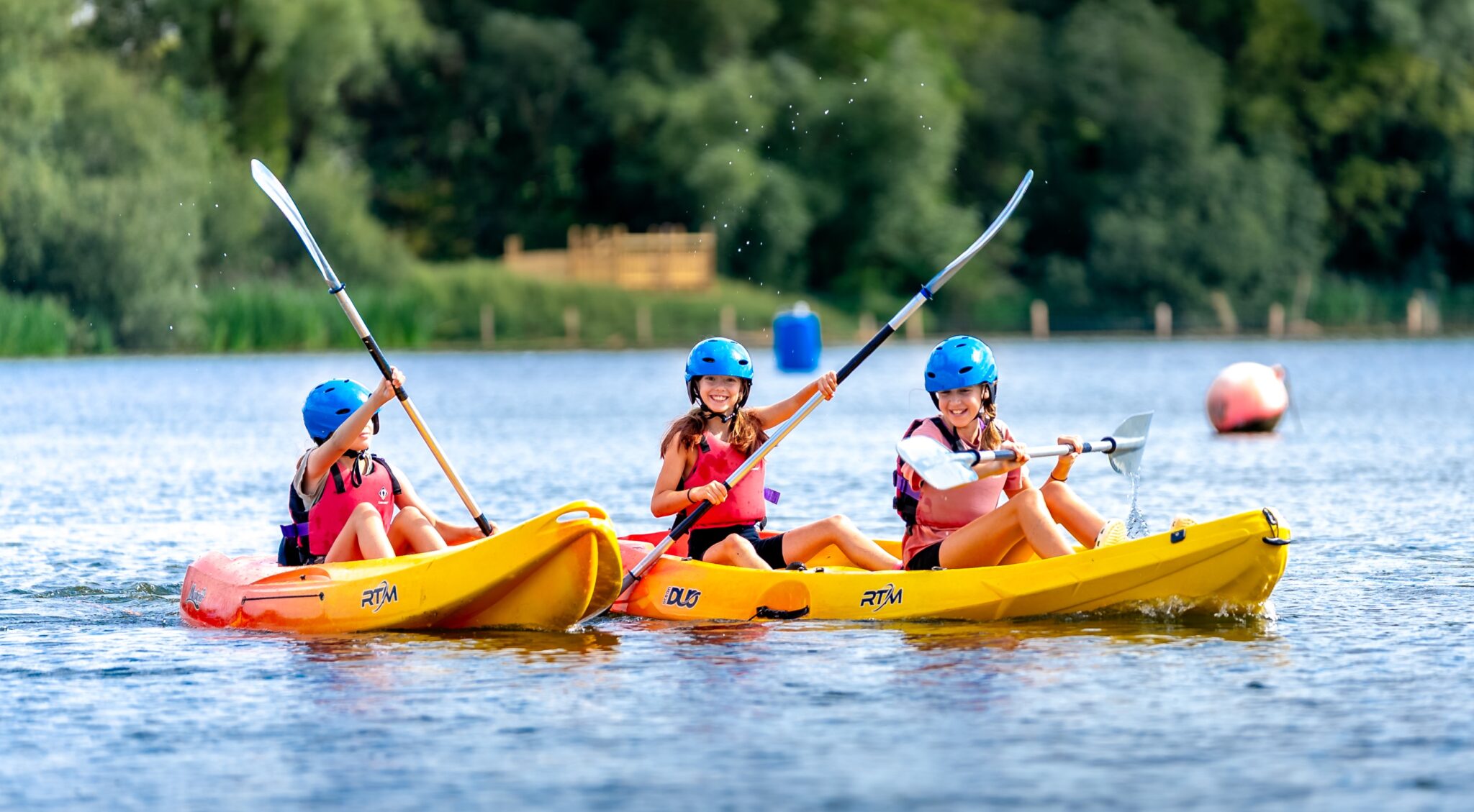 three girls in yellow kayaks on a blue lake on a sunny day