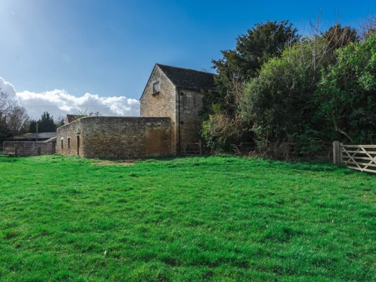 Old farm buildings behind a green meadow