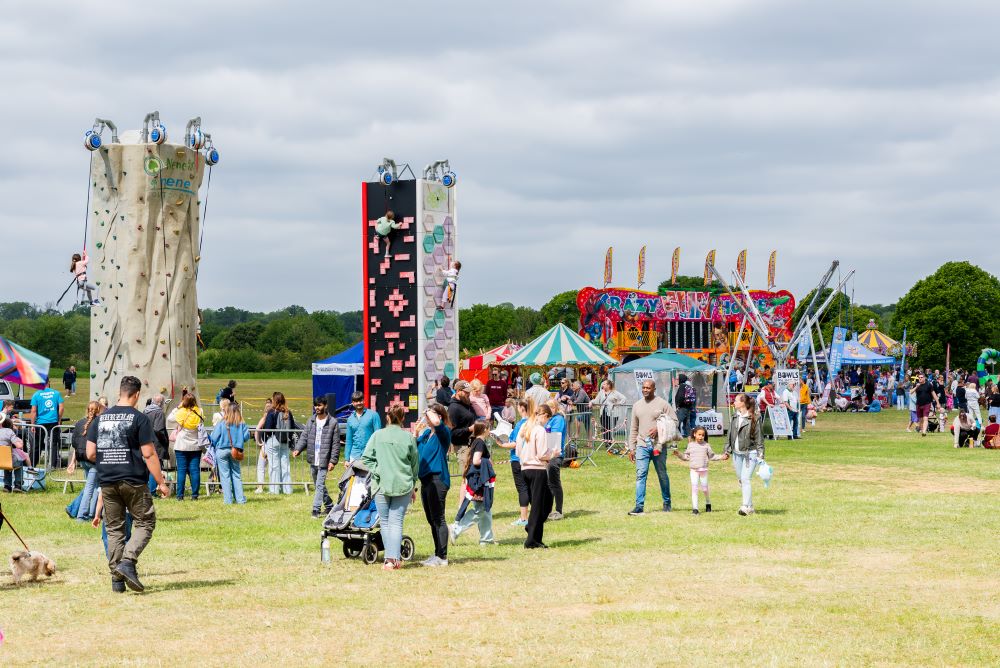 An outdoor festival in a field with climbing walls and fairground attractions