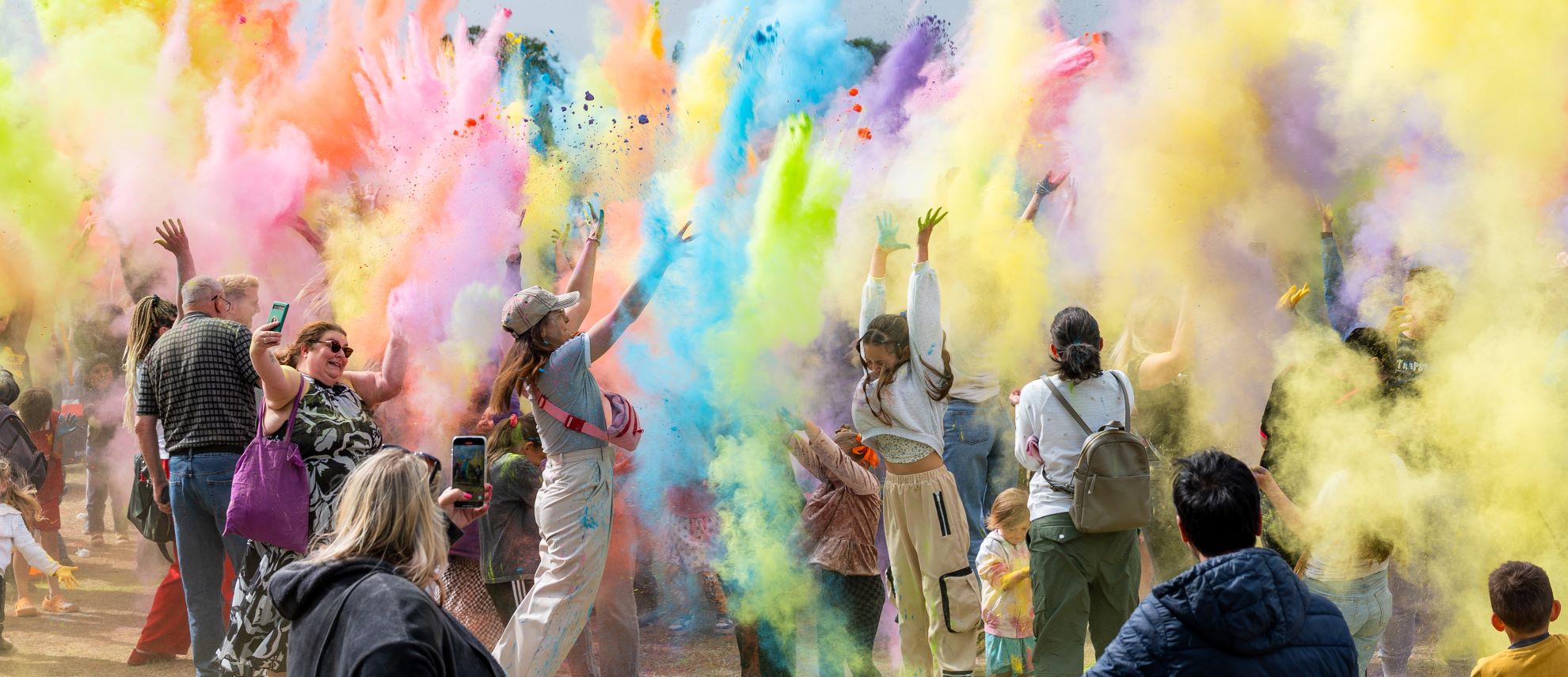 Scene showing people throwing coloured paint powder into the air as part of the Hindu festival Holi
