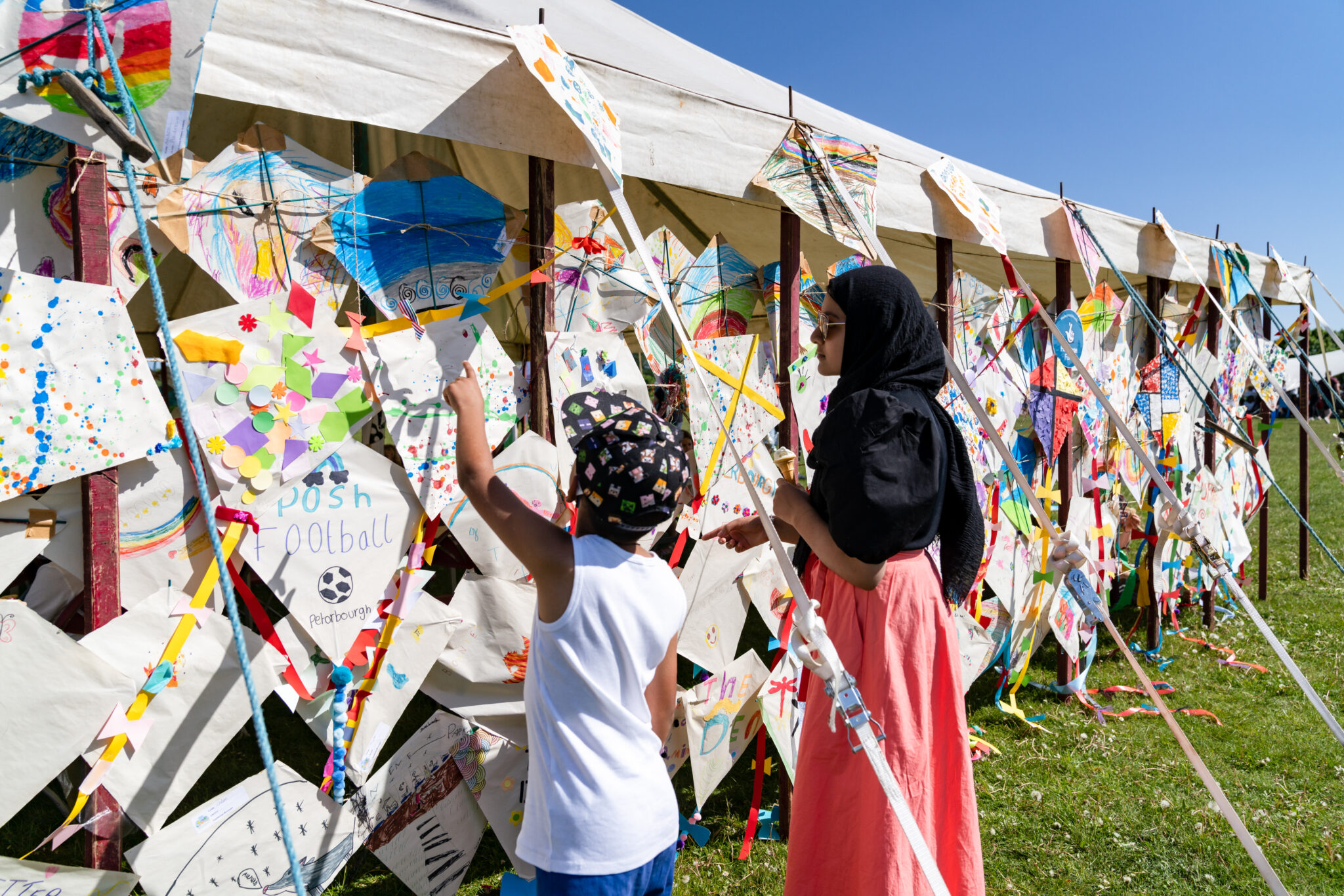 Two children looking at home made colourful kites displayed outside a marquee