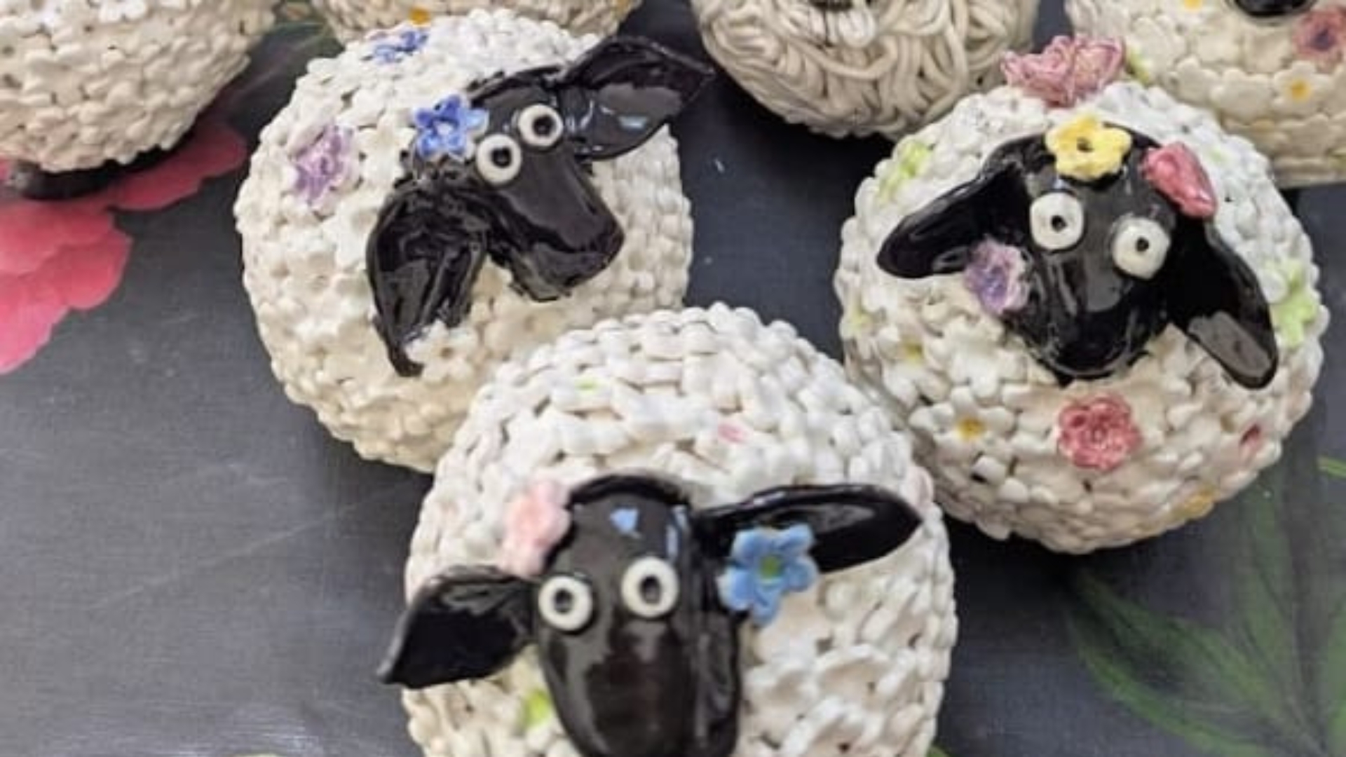 A selection of three, very round ceramic sheep. Each one has several different flowers in a variety of colours stuck to it.