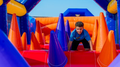 A young, primary school age boy crawls on all -fours across a large, vibrant inflatable obstacle course. He stares ahead, anticipating how to proceed, excitement etched on his face.