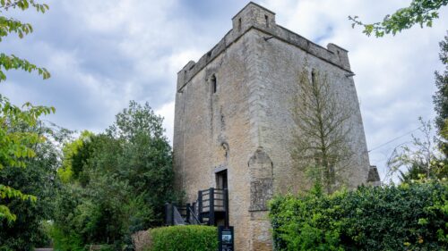 An exterior image looking upward at Longthorpe Tower, a medieval building dating back to the 14th century. It is surrounded by vibrant greenery and a slightly moody sky.