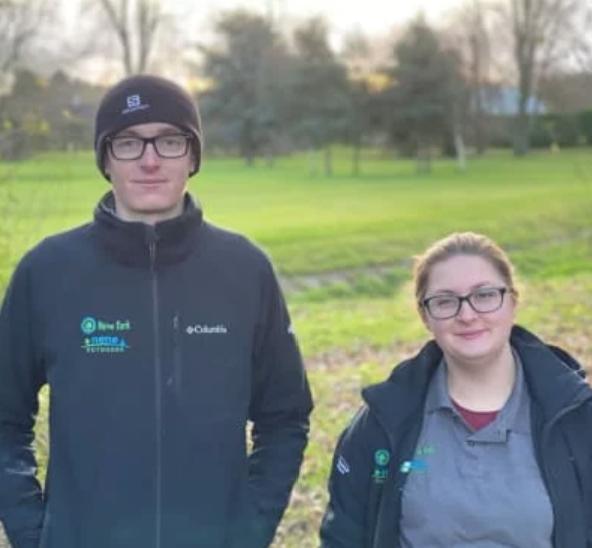 Two young people in Nene Park Trust uniform standing in a park.
