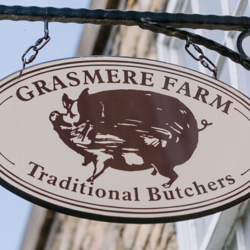 Grasmere Farm Traditional Butchers sign hanging on a stone shop wall