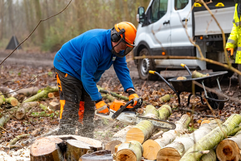 A man with a helmet, chopping wood with a chainsaw