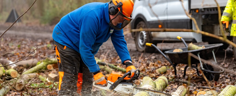 A man with a helmet, chopping wood with a chainsaw