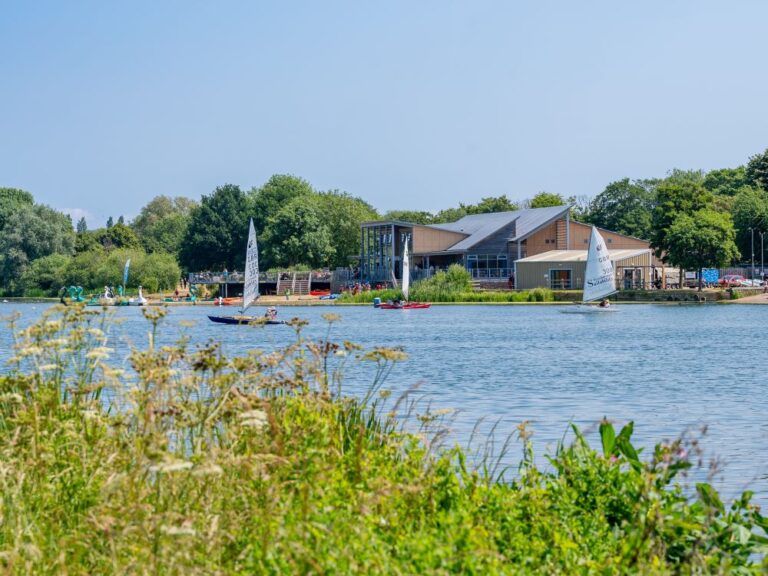 View across a lake of a watersports and sailing centre with people on the lake enjoying watersport activities